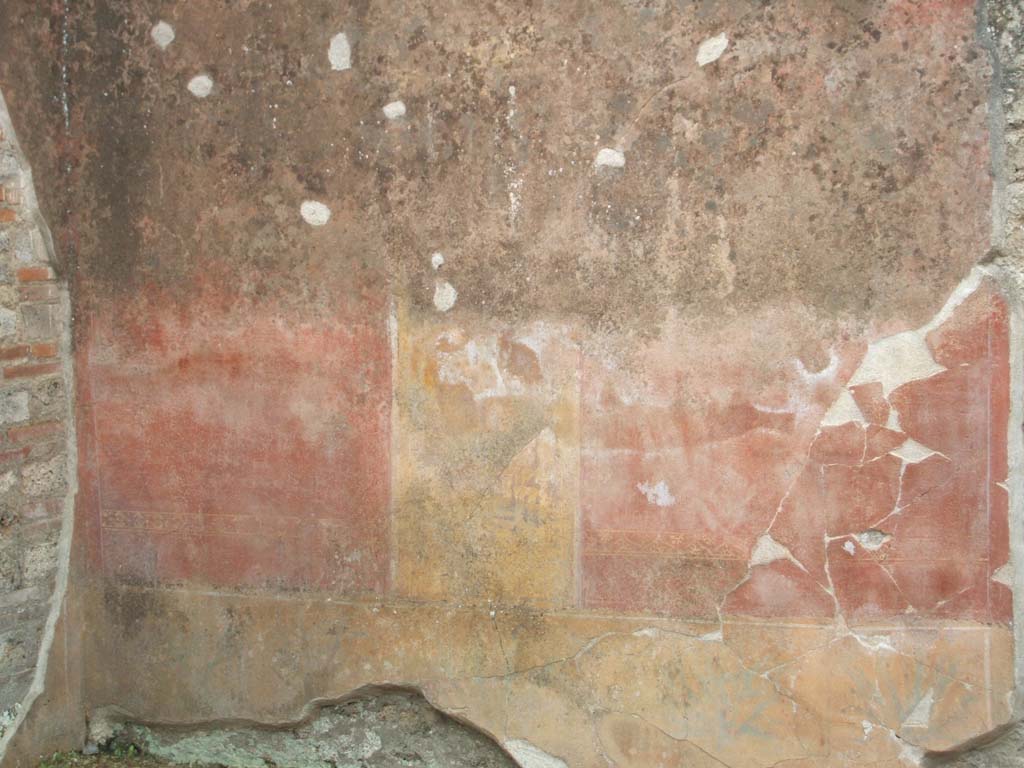 V.3.9 Pompeii. May 2005. West wall of site of room on the south side.
According to NdS, the south wall, on the left of the photo, was also divided into three panels.
The two side panels were red with a griffin and a flying tiger in gold.
The central panel was yellow and showed a painted closed door, framed by red and white pilasters with entablature.
In the middle was a painted door-knocker in the shape of an ox’s head.
Above this area, around the window that opened towards house V.3.8, there were other subtle architectural decorations in yellow on a red background.
Painted dolphins and other ornaments could be seen.
See Notizie degli Scavi di Antichità, 1902, dated November 1901, p.201-203.