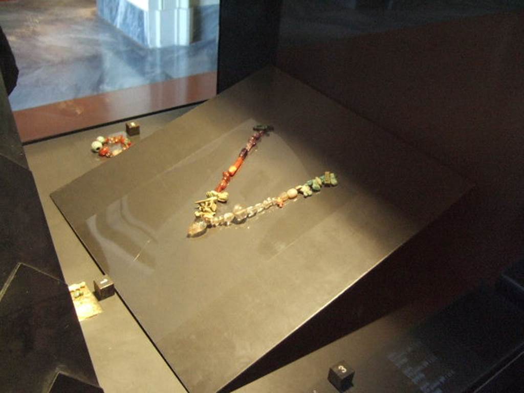 V.3.11 Pompeii. Necklace found in V.3.11. Now in Naples Archaeological Museum. According to Boyce, in the small room to the left of the entrance corridor were found the contents of a chest which had been destroyed. Many pieces of jewellery and 3 bronze statuettes were found. Two of the statuettes represented Harpocrates wearing the lotus flower upon his forehead and holding the index finger of his right hand to his lips. The third statuette was of Venus Anadyomene. See Boyce G. K., 1937. Corpus of the Lararia of Pompeii. Rome: MAAR 14. (Appendix 1, Item 2, p. 108) See Not. Scavi, 1902, 370.