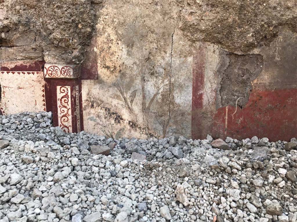 V.3.13 Pompeii. 2018. Room 2a. East wall. A sumptuous painted lararium begins to emerge from the lapilli in a room which was being excavated. 
On the left is the edge of the niche and right is painting of flowers.
Parete est. Un sontuoso larario dipinto inizia ad emergere dai lapilli in una stanza che è stata scavata. 
A sinistra è il bordo della nicchia e a destra è dipinto di fiori.
Photograph © Parco Archeologico di Pompei.