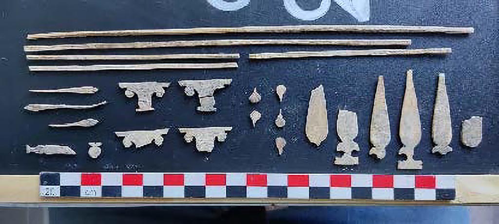 V.3.14 Pompeii. August 2022. Room 16. Letto 2.
Bone decorations of the head of the bed at the southeast corner of the room.
Decorazioni in osso della testata del letto presso l’angolo sud-est dell’ambiente.
Photograph © Parco Archeologico di Pompei.
The second bed, also 'high-backed' and with similar dimensions to the first, was placed in the south-east corner of the room, with an east-west orientation. This bed also shows a thick horizontal frame, with iron pins to lock its structure. At the height of the north-west foot, it was possible to recover some of the large iron pins pertaining to the frame, embellished by the presence of circular studs moulded in bone that masked their presence. At the moment, little can be reconstructed of the wooden structure; only its volume can be seen, as the piece of furniture was largely covered by the collapse of the false ceiling following the destructive events of AD 79, as well as being affected by the cutting of a tunnel that was evidently excavated a short time after the destruction. This bed also boasts the presence of wooden headboards on the two sides adjacent to the wall. In this case, the decoration is far more elaborate as it is embellished by the presence of very fine bone inlays. As many as seven millimetric shapes make up the decorative syntax of the panel, on three registers, from simple linear laths to elements in the shape of an Ionic capital, in the shape of a lanceolate leaf with two sepals below, and in the shape of a teardrop.
Il secondo letto, anch’esso “a spalliera alta” e con dimensioni simili al primo, era posto nell’angolo sud-est dell’ambiente, con orientamento est-ovest. Anche questo letto mostra un telaio orizzontale di grande spessore, con perni in ferro a bloccarne la struttura. All’altezza del piede nord-ovest è stato possibile recuperare alcuni dei grossi perni in ferro pertinenti all’intelaiatura, impreziositi dalla presenza di borchie circolari modanate in osso che ne mascheravano la presenza. Al momento si riesce a ricostruire poco della struttura lignea, se ne legge solo la volumetria in quanto il mobile è stato in gran parte coperto dal crollo del controsoffitto avvenuto in seguito agli eventi distruttivi del 79 d.C. nonché interessato dal taglio di un tunnel scavato evidentemente a poca distanza temporale dalla distruzione. Anche questo letto vanta la presenza delle testate lignee sui due lati in adiacenza al muro. In questo caso la decorazione è ben più elaborata poiché impreziosita dalla presenza di sottilissimi intarsi in osso. Sono ben sette le forme millimetriche che compongono la sintassi decorativa del pannello, su tre registri, dai semplici listelli lineari ad elementi a forma di capitello ionico, a forma di foglia lanceolata con due sepali sottostanti ed a forma di goccia.