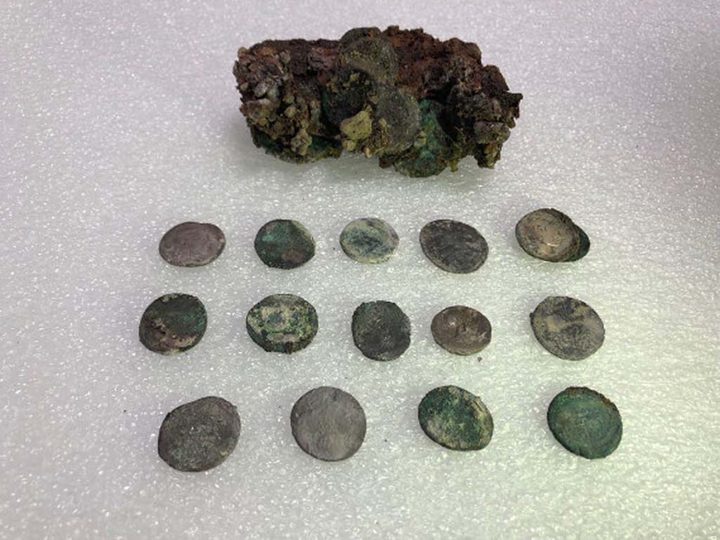 Regio V Pompeii. 2018. Leather pouch containing coins found under Pompeii skeleton in the Vicolo dei Balconi.
At first examination of the money found with skeleton of victim there would seem to be at least 20 silver denarii and two bronze asses for a nominal value of eighty sesterces and a half. 
Such a quantity of coins could at that time ensure the maintenance of a three-person family for 14, 16 days. 
The coins have very varied chronology. 
It was possible to examine 15 coins, for the main part Republican, starting from the Mid-second century B.C. 
One of the later Republican coins is a legionary denarius of Mark Antony, common in Pompeii, with the indication of the XXI Legion. 
Among the few Imperial coins identified, a probable denarius of Octavian and two denarii of Vespasian.
Borsa di cuoio contenente monete trovate sotto lo scheletro di Pompei nel Vicolo dei Balconi.
Al primo esame delle monete trovato con lo scheletro della vittima sembrerebbero esserci almeno 20 denari d'argento e due as di bronzo per un valore nominale di ottanta sesterzi e mezzo.
Una tale quantità di monete potrebbe quindi garantire il mantenimento di una famiglia di tre persone per 14, 16 giorni.
Le monete hanno una cronologia molto varia.
Fu possibile esaminare 15 monete, per lo più repubblicane, a partire dalla metà del II secolo a.C.
Una delle monete repubblicane più tardi è un denario legionario di Marco Antonio, comune a Pompei, con l'indicazione della XXI Legione.
Tra le poche monete imperiali identificate, un probabile denario di Ottaviano e due denari di Vespasiano.
Photograph © Parco Archeologico di Pompei.
