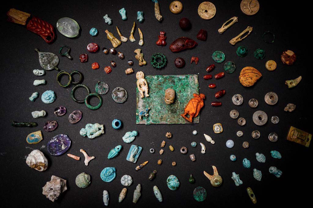 V.3 Pompeii. Casa del Giardino. August 2019. Amulets and gems for personal ornamentation or to protect against bad luck.
Amulets, gems and small objects re-emerge from the excavation of the Regio V. They were related to the female world, used for personal ornamentation or to protect from bad luck. They were found in one of the rooms of the House of the Garden. 
Kept in a wooden box, they have been restored and brought to their former glory by the restorers of the Laboratory of the Archaeological Park of Pompeii. They were probably objects that the inhabitants of the house could not take away before they escaped. The wood of the box has decomposed and only the bronze hinges remain, well preserved under the volcanic material.
Among the numerous objects found, two mirrors, pieces of necklace, decorative elements made of faience, bronze, bone and amber, a glass unguentaria, phallic amulets, a human figure and various gems (including an amethyst with a female figure and a carnelian with a craftsman figure). In a glass paste is engraved the head of Dionysus, on another a dancing satyr. The high quality of the amber and glass pastes and the engraving of the figures confirm the importance of the domus owner.
"They are objects of everyday life in the female world and are extraordinary because they tell micro-stories, biographies of the inhabitants of the city who tried to escape the eruption" - says General Director Massimo Osanna - "In the same house, we discovered a room with ten victims, including women and children, and now we are trying to establish kinship relationships, thanks to DNA analysis. Perhaps the precious box belonged to one of these victims. Interesting is the iconography of objects and amulets, which invoke fortune, fertility and protection against bad luck. And the numerous pendants in the shape of small phallus, or the ear, the closed fist, the skull, the figure of Harpocrates, the scarabs. Symbols and iconographies that are now being studied to understand their meaning and function"
See PAP: The-luck-and-the-protection-against-the-bad-fate-in-the-jewelery-of-regio-v
Amuleti e gemme per ornamenti personali o per proteggere contro la sfortuna.
Amuleti, gemme ed elementi decorativi in faience, bronzo, osso e ambra riemergono dallo scavo della Regio V. Erano monili e piccoli oggetti legati al mondo femminile, utilizzati per ornamento personale o per proteggersi dalla cattiva sorte, ritrovati in uno degli ambienti della casa del Giardino.
Custoditi in una cassa in legno, e da poco restaurati e riportati al loro splendore dalle restauratrici del Laboratorio di Restauro del Parco Archeologico di Pompei, si trattava di una parte dei preziosi di famiglia, che forse gli abitanti della casa non riuscirono a portare via prima di tentare la fuga. La traccia della cassa in legno che conteneva i reperti, le cui cerniere bronzee si sono ben conservate all’interno del materiale vulcanico, a differenza della parte lignea decompostasi, è stata individuata accanto all’impronta di un’altra cassa o mobile nell’angolo di uno degli ambienti di servizio, probabilmente usato come deposito.
 
Sul fondo dell’impronta sono stati rinvenuti i numerosi oggetti preziosi, tra cui due specchi, diversi vaghi di collana, elementi decorativi in faience, bronzo, osso e ambra, un unguentario vitreo, amuleti fallici, due frammenti di una spiga di circa 8 cm e una figura umana, entrambi in ambra, probabilmente dal valore apotropaico, e varie gemme (tra le quali una ametista con figura femminile e una corniola con figura di artigiano). Diversi pezzi si contraddistinguono per la qualità pregiata dei materiali, oltre che per la fattura. Tra le paste vitree, straordinarie sono quelle con incise, su una la testa di Dioniso, sull’altra un satiro danzante.
Alcuni oggetti preziosi sono stati rinvenuti anche in una altra stanza della casa, presso l’atrio, dove sono stati documentati i resti scheletrici di donne e bambini, sconvolti da scavi clandestini di età moderna (XVII – XVIII secolo), probabilmente finalizzati proprio al recupero dei preziosi che le vittime portavano con sé. Solo un anello in ferro, ancora al dito della vittima, e un amuleto di faience sono casualmente sfuggiti a questo saccheggio.
Considerate le straordinarie condizioni di conservazione e la particolare qualità dei manufatti è stato possibile donar loro una nuova vita mediante un intervento di semplice pulitura e consolidamento con materiali reversibili.
“Si tratta di oggetti della vita quotidiana del mondo femminile e sono straordinari perché raccontano microstorie, biografie degli abitanti della città che tentarono di sfuggire all’eruzione. – dichiara il Direttore Generale Massimo Osanna - Nella stessa casa, abbiamo scoperto una stanza con dieci vittime, tra cui donne e bambini, di cui stiamo cercando di stabilire le relazioni di parentela e ricomporre la biografia del gruppo familiare, attraverso le analisi sul DNA. E chissà che la cassetta di preziosi non appartenesse a una di queste vittime. Particolarmente interessante è l’iconografia ricorrente degli oggetti e amuleti, che invocano la fortuna, la fertilità e la protezione contro la mala sorte. E dunque i numerosi pendenti a forma di piccoli falli, o la spiga, il pugno chiuso, il teschio, la figura di Arpocrate, gli scarabei. Simboli e iconografie che sono ora in corso di studio per comprenderne significato e funzione”
See PAP: La-fortuna-e-la-protezione-contro-la-malasorte-nei-monili-della-regio-v
Foto: Cesare Abbate/ANSA courtesy Parco Archeologico di Pompei.
