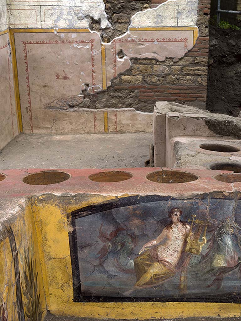 V.3 Pompeii, Thermopolium with painting of nereid. December 2020. Wall behind the counter decorated with panels bordered in yellow with still life in the centre.
V.3 Pompei, Termopolio con dipinto di nereide e anfore. Dicembre 2020. Parete dietro il bancone decorata con pannelli delimitati in giallo con natura morta al centro.
Photo by Luigi Spina courtesy of Parco Archeologico di Pompei.