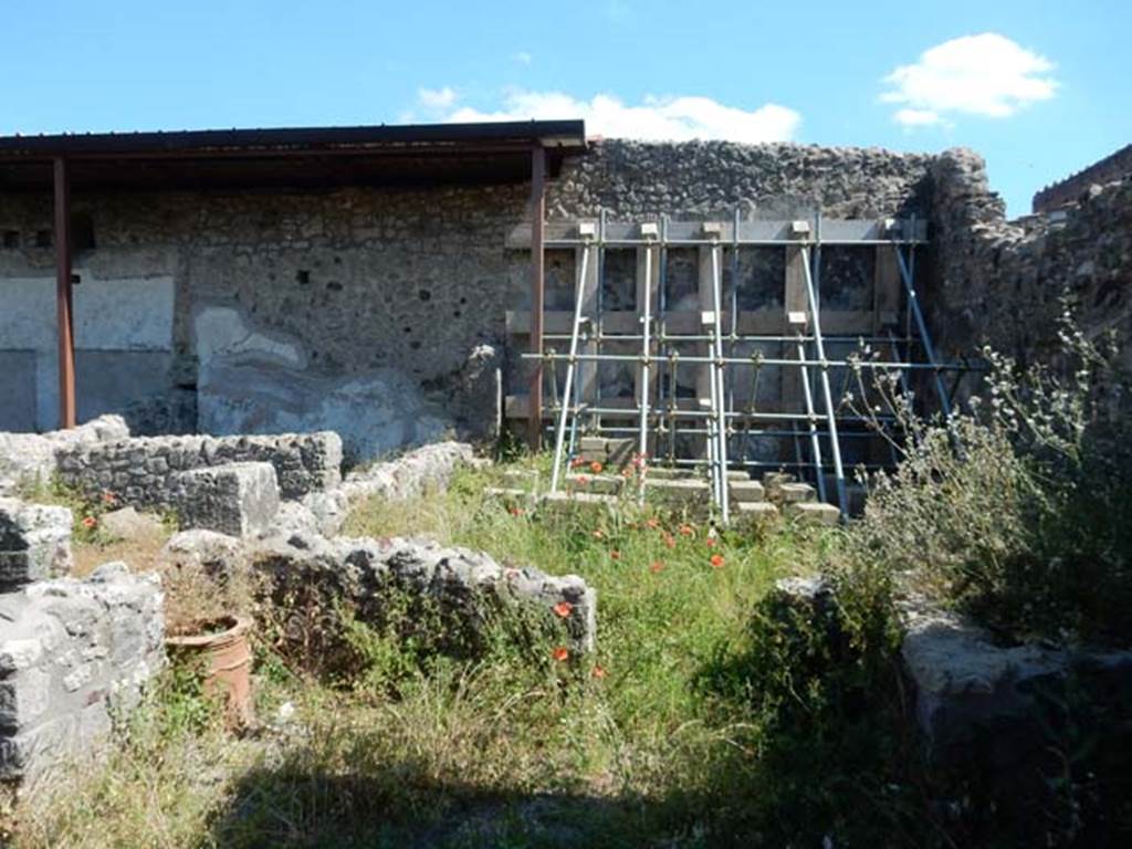 V.4.13 Pompeii. May 2017. Looking south towards garden wall, behind hoarding. 
The blocks of stonework could be forming the site of the triclinium and table !  Photo courtesy of Buzz Ferebee.
According to Soprano –
“Ubicazione: giardino. L. medius, m. 400; l. imus e l. summus, m.3.75; mensa m.1.50 per 0.90.
Bibliog. Thedenat, op. c. p.34; “Not. Scavi”, (1905), p.91.
Il Sogliano, descrivendo questo triclinio afferma trattarsi “di un basso sedile collocato intorno ai tre lati di una mensa e col quale si volle ricordare la disposizione dei letti tricliniari in muratura”. Parmi, peraltro, piu esatto riconoscere in questo “sedile” l’impianto di un vero triclinio.
L’esistenza di fori circolari nel terreno attesta che il triclinio era ombreggiato da un pergolato.
I letti laterali sono di eguale lunghezza. La mensa rettangolare, attualmente grezza, era originariamente rivestita di intonaco e ricoperta da una lastra di marmo colorato.”
See Soprano, P. (1950). I triclini all’aperto di Pompei. (In Pompeiana, raccolta di studi per il secondo centenario degli scavi di Pompei. Napoli, Gaetano Macchiaroli, Editore, P. 299, no.12).