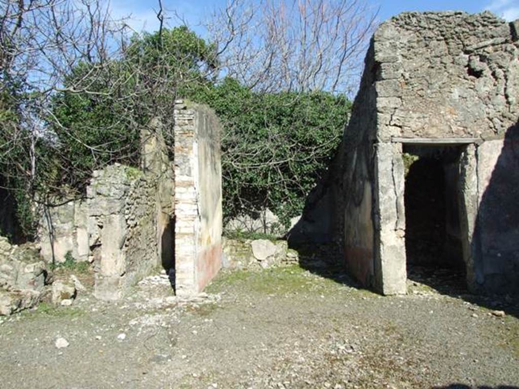 V.4.c Pompeii. March 2009. Room B, the atrium, looking east. Looking across atrium to doorways to room F, on left, room J, corridor to garden, room G, tablinum, and room H, cubiculum.  When excavated the atrium had flooring similar to that of the fauces, opus signinum/cocciopesto.
V.4.c Pompeii (described as second house after that of Lucrezio Frontone).
Found on 15th March 1902, between the upper layers of a room near the tablinum, was an oxidised statuette (100mm high) of a bearded and crowned Hercules, leaning with the weight of his body on his right leg, since the left leg was slightly bent. In his right hand he held the club pointing downwards, and in his left hand he held the apples of the Hesperides; the lion’s skin was hanging on his left forearm. If he was beardless, he would have very closely resembled the Hercules Righetti of the Vatican Rotunda. Also found were – a bronze cylindrical bell with an iron ringer/clapper. An oxidised medium and small bronze coin. A glass bottle with a spherical belly. Found on the 24th March in the same place was a terracotta single-burner lamp, with a ring handle. See Notizie degli Scavi di Antichità, 1902, (p.213)
