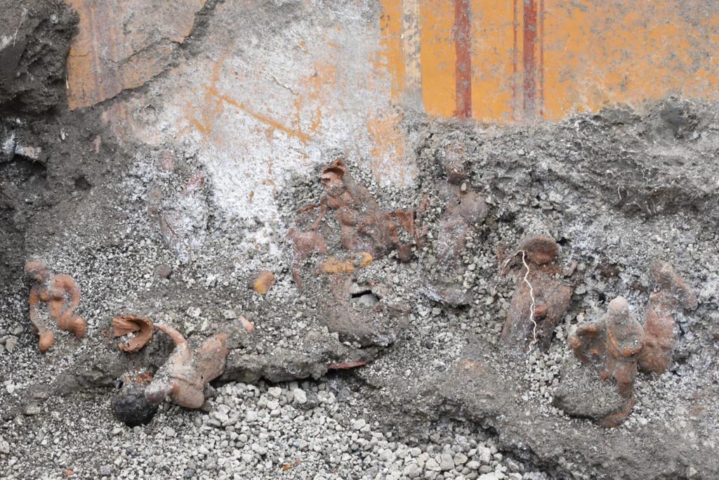 V.6.13 Pompeii. December 2023.
Amb. 42-43 scavo della nicchia del larario che mostra le statuette votive in terracotta.
L’11 dicembre del 2023, al di sotto di una coltre di lapillo, all’interno di una nicchia ricavata nella parete N-S dell’ambiente 42, sono state rinvenute 13 statuine in terracotta, di circa 15-20 cm, realizzate con matrici bivalve e caratterizzate da una vivace policromia. Esse sono state ritrovate schierate su un asse orizzontale in posizione eretta, all’interno di un vano definito da blocchi di travertino, dove presumibilmente si trovava un mobile scaffale (fig.10). In realtà, il recupero di molti altri frammenti denota la presenza di una teoria di sculture senz’altro più copiosa (fig.11-12-13). Oltre figure antropomorfe, si riconoscono una noce, una mandorla, la testa di un gallo in argilla, una pigna in vetro
Amb. 42-43 excavation of lararium niche showing the terracotta votive statuettes.
On 11 December 2023, 13 terracotta figurines, measuring approximately 15-20 cm, made of bivalve moulds and characterised by a vivid polychromy, were found under a layer of lapilli, inside a niche in the N-S wall of room 42. They were found lined up on a horizontal axis in an upright position, inside a room defined by travertine blocks, where a mobile shelf was presumably located (fig. 10). In reality, the recovery of many other fragments denotes the presence in theory of sculptures that are undoubtedly more copious (fig.11-12-13). In addition to anthropomorphic figures, one recognises a walnut, an almond, the head of a rooster in clay, a glass pine cone.
Vedi/See E-Journal 09: 22.12.23, Scavo e restauro della Casa di Leda – Regio V, 6. Nuovi rinvenimenti, p. 5-6, fig. 10.
Photograph © Parco Archeologico di Pompei.
