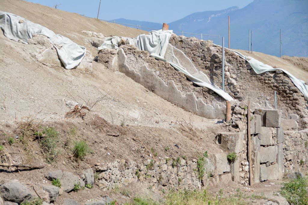 V.6.15 and V.6.14, Pompeii. 2018. Looking south along front facades on east side of Via del Vesuvio during works. 
Photo © Parco Archeologico di Pompei.
(c.2018-2019). In order to improve the drainage and security for visitors to the site, the soil, ash and exuberant vegetation was removed from the slope of the unexcavated land on the east side of Via del Vesuvio (Insula V.6).
This has cleared the area to enable the street boundary wall and rooms at its immediate rear to be viewed from Via del Vesuvio.