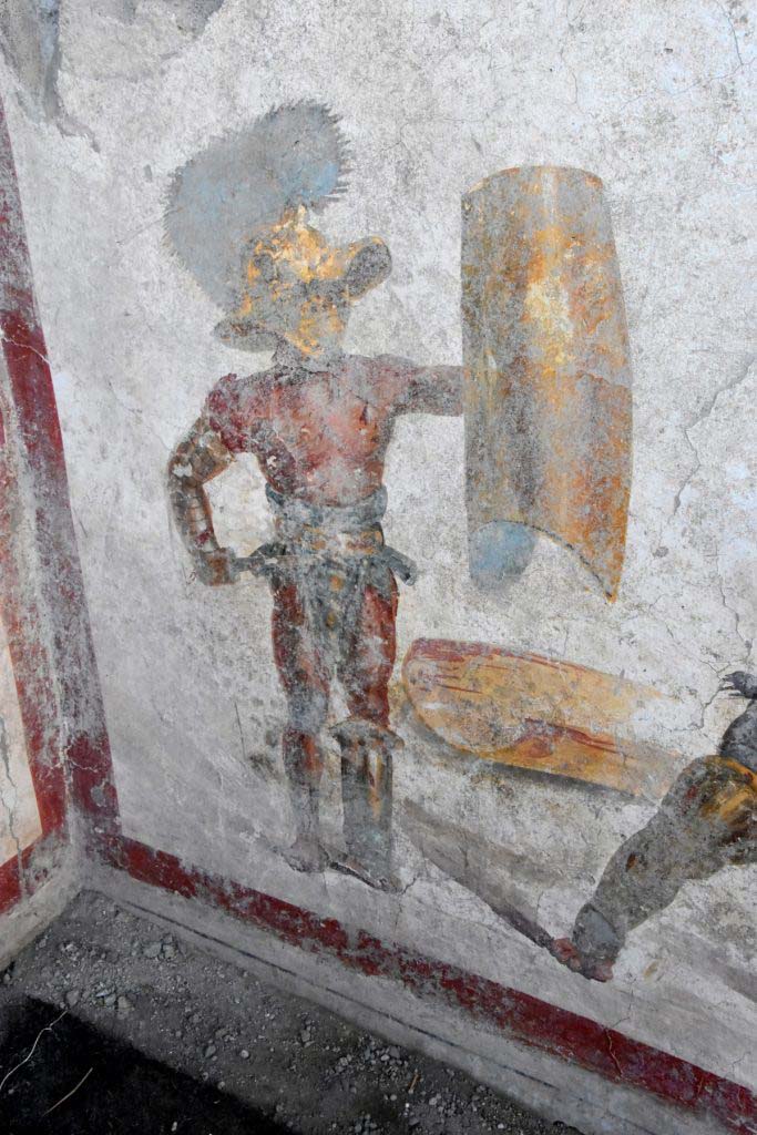 Detail of the "Mirmillo" of the "Scutati" category: he wields the offensive weapon, the gladium, (short Roman sword) and a large rectangular shield (scutum) and wears a wide-brimmed helmet equipped with visor with plumes, the cimian. 
Dettaglio del “Mirmillone” della categoria degli "Scutati”: impugna l’arma di offesa, il gladium, (corta spada romana) e un grande scudo rettangolare (scutum) e veste un elmo a tesa larga dotato di visiera con pennacchi, il cimiero.
Photograph © Parco Archeologico di Pompei.