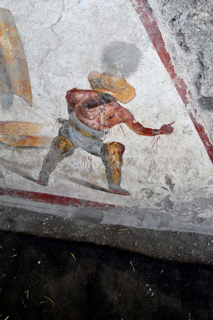 The other, in a succumbing position, is a "Thracian", a gladiator of the "Parmularii" category, with the shield on the ground. 
He is represented with a helmet (galea), with wide brim and wide visor to protect the face, topped by a tall crest.
L’altro, in posizione soccombente, è un “Trace”, gladiatore della categoria dei "Parmularii”, con lo scudo a terra. È rappresentato con elmo (galea), a tesa larga ed ampia visiera a protezione del volto, sormontato da un alto cimiero.
Photograph © Parco Archeologico di Pompei.