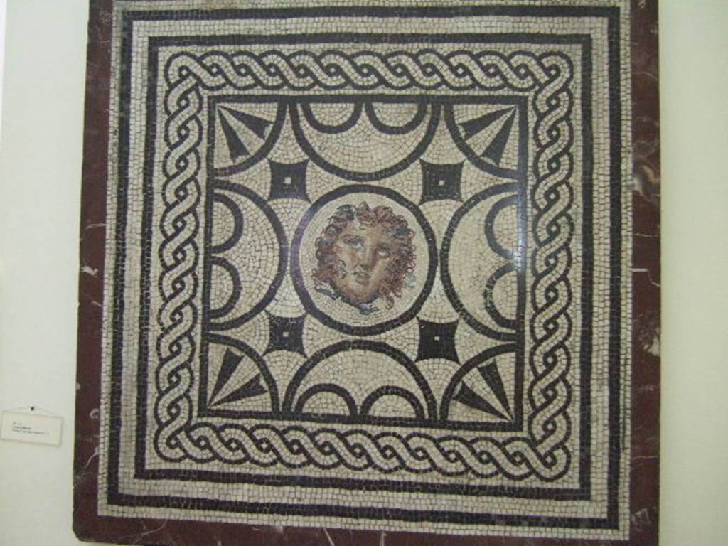 Found in VI.1.7 Pompeii. Mosaic with head of Medusa. 
Now in Naples Archaeological Museum. Inventory number s. n.
According to Pagano and Prisciandaro –
11 Novembre 1784, Cubicolo – 
“Si continua a scavare nella consaputa abitazione, e si e scoperta una stanza. Questa tiene il pavimento di musaico bianco, ed il piano suo vien distinto da un grado alto on.6. Tale altezza e ornata da un fascia di marmo, ed il detto piano superiore e di musaico liscio. E nel piano sottoposto vi e un quadro con dei lavori di musaico nero, e nel centro vi e una testa bellissima di Medusa anche di musaico. Le mura di questa stanza sono cosi dipinte: lo zoccolo giallo con alcuni lavori, il dippiu bianco con riquadrature di fasce rosse con varie pitture, festoni ed altro. Vi si e trovato – Bronzo: Una lucerna ad un luminello e suo manico. Un piccolo anelletto. Due chiodi ed una centrella. Osso: Un netta orecchie.”
See Pagano, M. and Prisciandaro, R., 2006. Studio sulle provenienze degli oggetti rinvenuti negli scavi borbonici del regno di Napoli. Naples: Nicola Longobardi.  (p.82 and see PAH,1,2,24 and Addendum p.40 (Il mosaico fu tagliato il 13 Decembre 1787).
(translation – 11th November 1784, Cubiculum –
"We continued to dig in the known house and found a room.  
This room had a white mosaic floor, and the floor was distinguished by a high step of 0.13m (approx. 5 inches high). 
This height was decorated by a strip of marble, and the said upper part of the floor was of smooth mosaic.  
And in the floor below, there was a picture worked with black mosaic, and in the middle there was a beautiful head of Medusa, also in mosaic. 
The walls of this room were painted: with a yellow zoccolo, with panels separated by red bands with various paintings, garlands and more. 
Bronze and bone items were found."
(Addendum: the mosaic was cut and taken to the Museum on 13th December 1787). (see below – sent on 21st December 1787).
PAH, 1787, p.40 –
13th Decembre 1787.
Si e mandato ad avvisare a Canart, che mandi a tagliere li due quadri di musaico, secondo ordino il sig. Ajutante D. Pietro La Vega. 
Uno e quello con la testa di Medusa di pal 3 ed on.8 in quadro; l’altro e quello con lo scheletro, che tiene in ciascuna mano, un vaso con la bocca inclinata verso la terra, di pal. 2 ¾ per pal. 2 ed on.5.
21st Decembre 1787.
Si sono mandati questa mattina pel R. Museo a D. Giuseppe Canart i due quadri di musaico, notati nel passato rapporto.
(translation - 13th December 1787.
One has sent to advise Canart to cut the two mosaics, according to the orders of La Vega.  One is the one with the head of Medusa of 0.97m squared;  
the other that with the skeleton holding a vase in each hand with the mouth tilted towards the earth, 0.73m x 0.64m. 
21st December 1787.
This morning, one has sent the two squares of mosaics, noted in the past report to the Royal Museum to D. Giuseppe Canart.)
(Note – the mosaic of the skeleton with the vase in each hand was excavated from VI. Ins. Occ. 25).