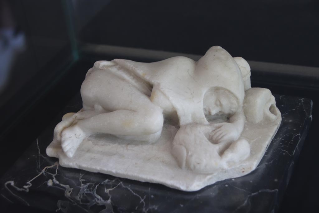 VI.2.22 Pompeii. October 2022. Marble statue described as “Young fisherman asleep”, found in the house but location unknown. 
On display in the Palaestra. PAP Inventory number 21628. Photo courtesy of Klaus Heese.
According to Jashemski –
“The two marble statuettes found in the house would probably have been garden decorations: a deer suckling her young (0.21m long) and a sleeping child whose left hand holds the handle of a basket which a mouse tries to enter. Behind the boy’s head an overturned vase (0.19m long) poured water.  The mask found in the house may also have decorated the garden.”
See Jashemski, W. F., 1993. The Gardens of Pompeii, Volume II: Appendices. New York: Caratzas. (p.122-3)