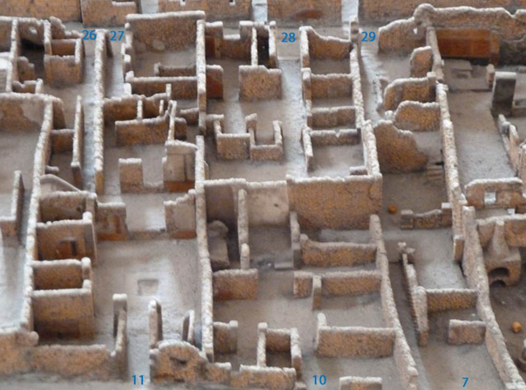 VI.2.29 Pompeii, in top right corner. Viewed from the model in the Naples Archaeological Museum.
According to Dyer: “This small house in the Vicolo di Modesto had neither atrium nor peristyle; but in order to enable the family to enjoy the fresh air which the richer classes obtained in those courts, a stone bench ran along the front of the house. The street door by the side of it opened into a sort of covered hall. On the left some stairs led to an upper storey, behind which there was a small room apparently for the slave. On the right hand side was an uncovered passage, with a well at the end of it, running along the greater part of the house; on the left of which is what appeared to have been a workshop, with a doorway from the entrance hall and lit by small windows from the uncovered passage. This room was followed by a dining-room entered by a doorway from the same passage, and behind this again, quite at the furthest extremity of the house, a kitchen, as may be recognised by the hearth. The sleeping rooms must have been upon the upper floor.”
See Dyer, T., 1867. The Ruins of Pompeii. London: Bell and Daldy. (p.74)