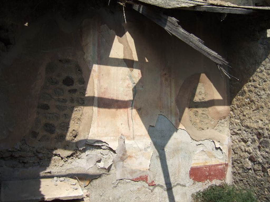 VI.5.7 Pompeii. September 2005. Remains of painted plaster in cubiculum nearest the north-east corner. The zoccolo would have had alternating panels of plants on a red background, and then narrow compartments with painted imitation marble. Above the zoccolo was a green painted predella, with a still-life at its centre. In the centre of the wall would have been a wide yellow aedicula painted with surrounding architectural columns.
