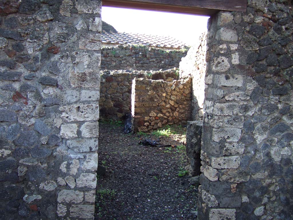 VI.5.14 Pompeii. December 2005. Looking west through doorway into kitchen area
The walls of the latrine can be seen in north-west corner.
The north-west corner of this room, the latrine, shows that today there is no doorway of VI.5.11 here, as shown on Eschebach plan.
VI.5.11, steps to an independent upper floor, is now to the north of this corner, fronting onto Vicolo di Modesto, and is completely separate from here.
According to CTP, the north-west corner of the house at VI.5.14 was excavated in 1817, as well as the pseudoperistyle of VI.5.10 and atrium area of VI.5.9.
The street wall at the north-west corner of the house at VI.5.14 collapsed and was reconstructed, which may provide the reason why Tascone, Mau and Eschebach, all indicated a rear doorway of this house immediately south of the stairway, which, rightfully should be assigned a number. 
The doorway is delineated by Russo’s map of 1817, and later by Mazois, Fiorelli – Sorgente, and Zangemeister (1865). 
Today the number VI.5.11 is not in situ but it has been assigned by the SANP to the staircase. 
See Van der Poel, H. B., 1981. Corpus Topographicum Pompeianum, Part V. Austin: University of Texas. (p.196-7)
