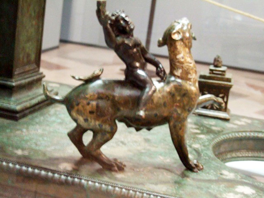 Bronze statuette of Dionysus mounted on his panther on the base of a candelabrum. 
A small altar is in the background. Found in VI.6.1 Pompeii. Now in Naples Archaeological Museum.