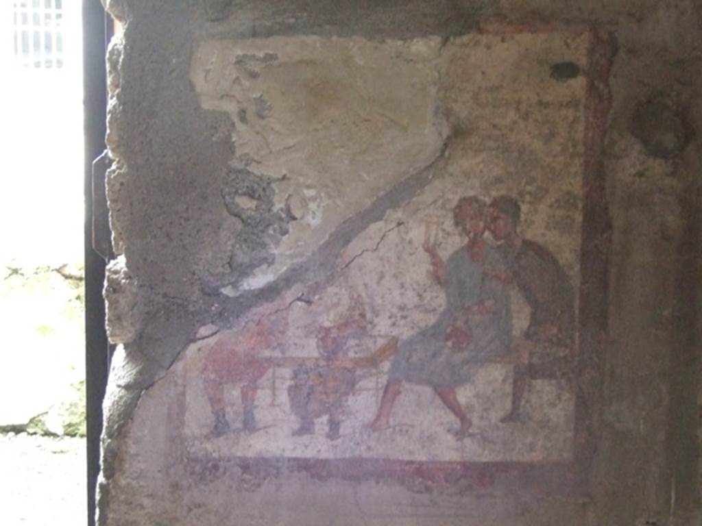 VI.10.1/19 Pompeii. March 2009. Fresco on west wall of rear room, on north side of doorway. 
Two men in tunics and wearing shoes sit at a table.  
A man in a blue tunic sits on a bench and a man in a brown tunic leans over him.  
See Helbig, W., 1868. Wandgemälde der vom Vesuv verschütteten Städte Campaniens. Leipzig: Breitkopf und Härtel. (1504; p369).