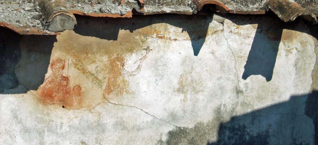 VI.11.9 Pompeii. September 2005. Room 16, detail of figures on lararium.
Household lararium showing Venus Pompeiana, Amor or Eros, and a Lar. A garland can be seen above.
According to Boyce, in the upper zone there used to be two Lares, Vesta and Venus Pompeiana.
Vesta had a wreath upon her head from which a white veil hung down her back.
On each side of her stood a Lar, clad in yellow tunic with green border.
To the left of this group of three stood Venus Pompeiana wearing red chiton and mantle and having on her head a mural crown.
To her left, between her and the Lar, was Amor, wearing an orange chlamys.
In the middle zone, a single serpent moved towards an altar painted at the left edge of the picture.
In the lowest zone lay the figure of the river Sarnus.
See Boyce G. K., 1937. Corpus of the Lararia of Pompeii. Rome: MAAR 14. (p.51, No.185, Pl.21, 1).
