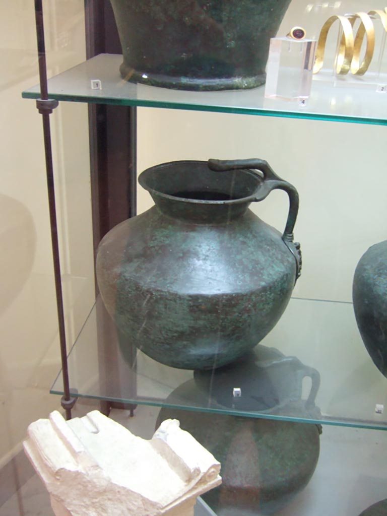 VI.12.2 Pompeii. One handled bronze jug, with small limestone altar, below. 
Now in Naples Archaeological Museum. Inventory number 69425.
The small altar (second half of the 2nd century BC), found 1831, now in Naples Archaeological Museum. Inv. 2550 (Vetter 21), with Oscan inscription, written from right to left, reading –
“To flora”
(Piccola ara (seconda metà del II secolo a.C.), trovato 1831, inv. 2550 (Vetter 21), alfabeto osco, scrittura da destra verso sinistra –
“A Flora”)
According to the information card in Naples Museum –
“Flora is one of the minor deities connected to the regenerative cycles of nature. Her cult was diffused through the Italic world, and is attested in Rome as well”.
(“Flora è una delle divinità minori legate ai cicli rigenerativi della natura, il cui culto era diffuso nel mondo italico e si ritrova anche a Roma.”)