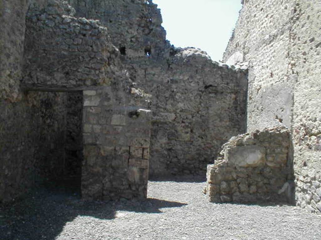 VI.14.24 Pompeii. May 2005. Looking west across shop to doorways to two rear rooms.
According to BdI, on the right of the shop entrance in the north-east corner, was a small hearth, and in the same corner was a latrine. Objects found in the shop were a bell, various pots, five keys and a few bronze coins. The rear room on the right was the biggest. 
Upon excavation, the walls of the upper rooms were also preserved, one above the rear rooms, the other above the shop-room. This last wall, with pink coloured plaster until the height of approximately 1.50m, unpainted above, and with a large window onto the roadway.  It was evident that these two rooms joined by a doorway between them, formed a separate complex from the rest of the house, and that this could be rented independently from the shop below. See Bullettino dell’Instituto di Corrispondenza Archeologica (DAIR), 1876, (p.44)