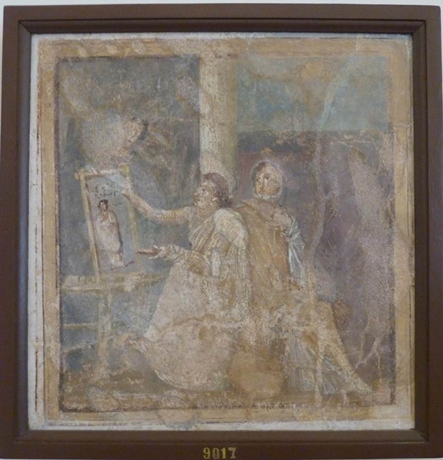 VI.14.42 Pompeii.  Found in Cubiculum (3), the room on the south (or right) of the entrance corridor.   Wall painting of woman painting.  
She holds a palette in her left hand and is painting a picture on a table or easel with the right.  A woman in yellow, with a white mantel over her shoulder, sits next to her. The woman admires the painting which is of a woman in a yellow robe. Now in Naples Archaeological Museum.  Inventory number 9017. See Helbig, W., 1868. Wandgemälde der vom Vesuv verschütteten Städte Campaniens. Leipzig: Breitkopf und Härtel. (1444). See Richardson, L., 2000. A Catalog of Identifiable Figure Painters of Ancient Pompeii, Herculaneum. Baltimore: John Hopkins. 
(p.120, he described it as a Genre scene with woman painting a picture, found in cubiculum 3, south of fauces).