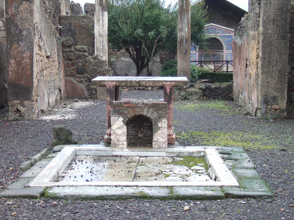 VI.14.43 Pompeii. December 2005. Room 1, impluvium in atrium, marble table and marble covered brick base or fountain.
According to Jashemski, unique so far at Pompeii, is the tiny mosaic fountain (about 0.50m high) in the atrium.
It had been built on the east edge of the impluvium, facing the entrance during the last years of the city. 
According to Sear, the front and bottom of the inside walls were lined with marble. 
Above this there was a “line of shells and then a zone of mosaic, in white, yellow, and blue, and above the mosaic another line of shells”.  
The head of the niche was covered with pumice and marine deposits.
See Jashemski, W. F., 1993. The Gardens of Pompeii, Volume II: Appendices. New York: Caratzas. (p.152)