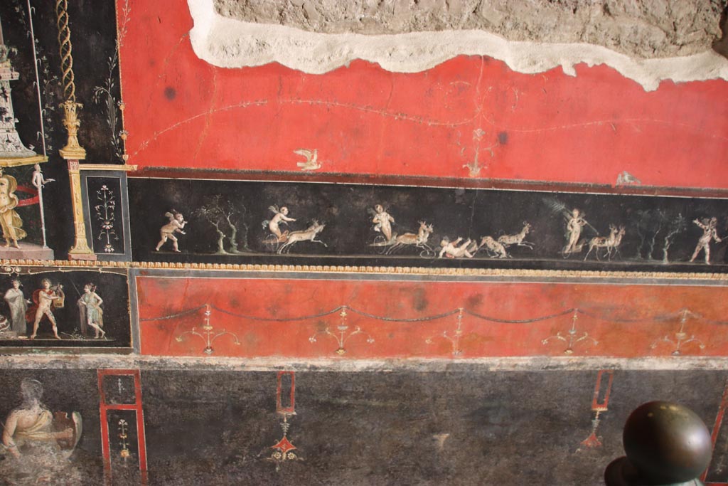 VI.15.1 Pompeii. October 2023.
Central panel in predella on east wall with painted panel of cupids in a race between chariots pulled by deer. Photo courtesy of Klaus Heese.