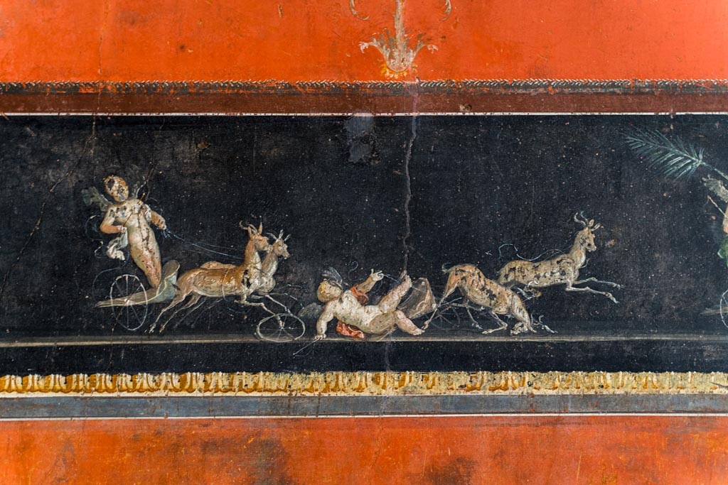 VI.15.1 Pompeii. March 2023.
Lower centre of east wall, detail of part of painted panel with cupids in a chariot race. Photo courtesy of Johannes Eber.