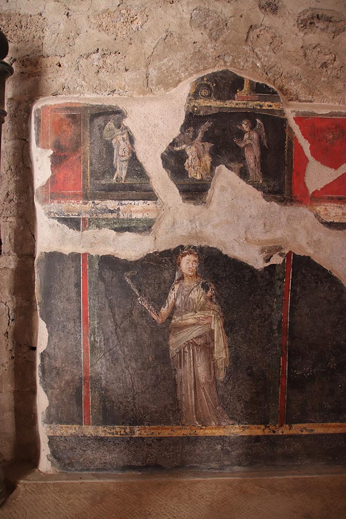 VI.15.1 Pompeii. October 2024.
West wall at south end. The wall painting above is of three Psychai gathering flowers.
Below is a female figure or priestess holding implements of sacrifice.
Photo courtesy of Klaus Heese.