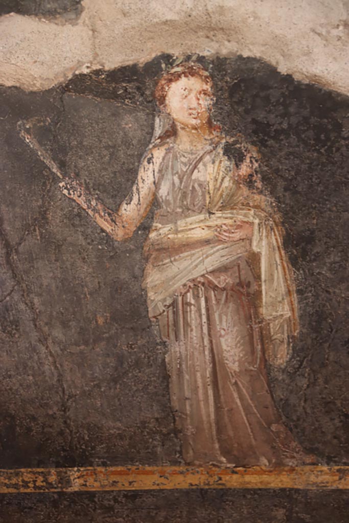VI.15.1 Pompeii. October 2023.
West wall at south end, painting in zoccolo of female figure or priestess holding implement of sacrifice.
Photo courtesy of Klaus Heese.