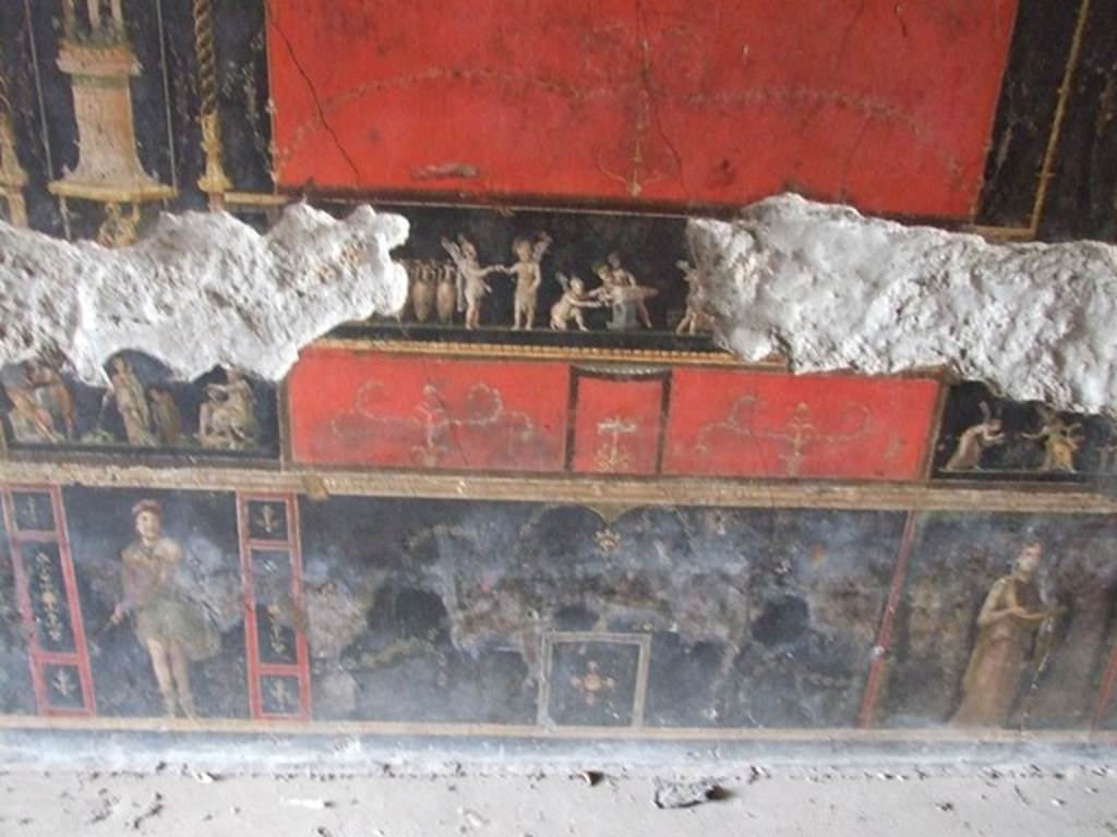 VI.15.1 Pompeii. December 2006. Central panel in predella on west wall, with painting of cupids buying and selling wine.
Underneath left is a standing figure of an Amazon armed with a shield.
Underneath right is a standing female figure or priestess holding implements of sacrifice.