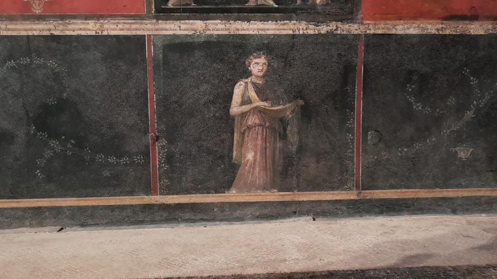 VI.15.1 Pompeii. January 2023.
Detail from zoccolo of west wall at north end with painting of female figure or priestess holding implements of sacrifice.
Photo courtesy of Miriam Colomer.