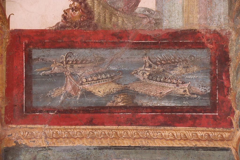 VI.15.1 Pompeii. October 2024.
Painted panel of naval scene on west side of central painting on south wall. Photo courtesy of Klaus Heese.