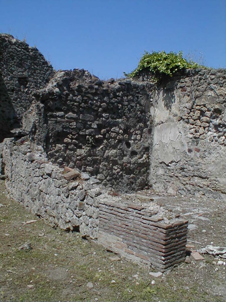 VI.15.3 Pompeii. May 2005. Room on north side of workshop, looking towards north-west corner.
According to NdS, the doorway from the workshop led into a spacious rustic room with a brick-plaster dado.
Some polychrome terracotta panels were fixed in the dado with iron nails (into the thickness of the plaster).
Each showed a cupid in a chariot in bas-relief.
Three of these remained, two on the north wall and one on the west wall.
They were 0.29m high and wide, representing a cupid on a galloping chariot. 
The cupid was standing in the chariot with both hands on the reins and bending forward to incite the horses in the race.
All the three panels were identical, varying only in the colour which was very poorly preserved. 
Almost in the centre of the north wall of the same room, on the same brick-plaster dado, Sogliano could make out traces
of figures painted onto the natural background.  
The deplorable state of the preservation made it impossible to see much, but on the left there were two male figures (0.27m high), and towards the centre of the wall there was possibly a female figure, the head of another figure could just be seen at shoulder level of the female figure.
See Notizie degli Scavi di Antichità, January 1897, (p.21).