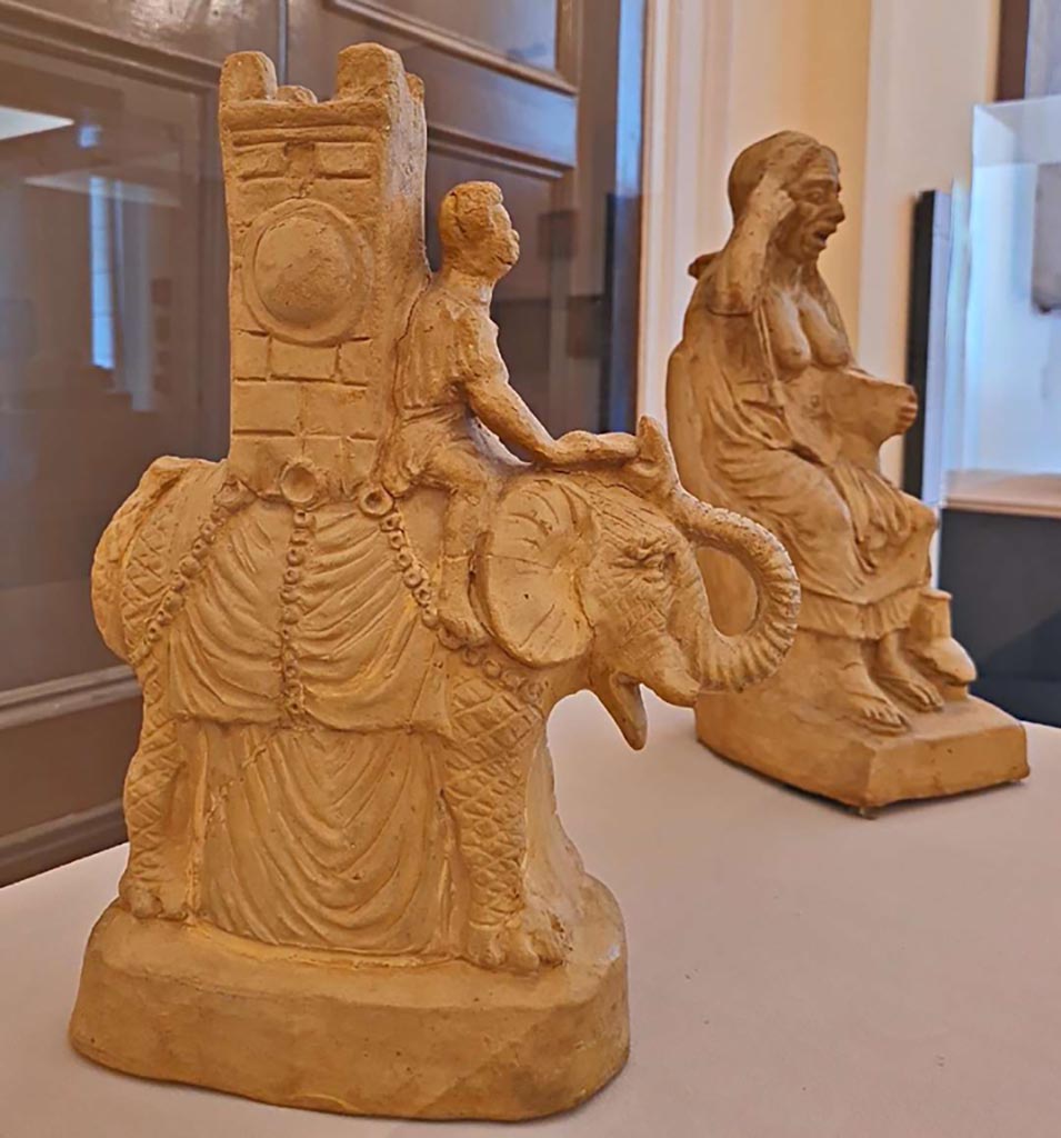 VI.15.5 Pompeii. October 2023. 
Clay figurine of an elephant carrying a tower on its back inv. 124845, and clay figurine of an old drunken woman inv. 124844. Photo courtesy of Giuseppe Ciaramella. 
On display in “L’altra MANN” exhibition, October 2023, at Naples Archaeological Museum.