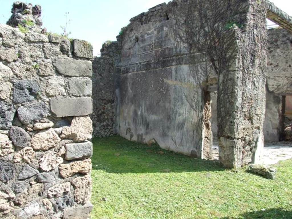 VI.15.5 Pompeii. March 2009. Doorway to room 24, oecus. South wall, with small door into tablinum. According to NdS, this room was a cubiculum and had a floor (“alla veneziana”) and was decorated in the First Style. On the south wall was the remaining decoration of a previous time showing stucco ashlars. Afterwards, a decoration of yellow panels divided by white areas with candelabra was substituted. The dado was on a black background with the usual concepts of marsh plants. See Notizie degli Scavi, January 1897, (p.27)