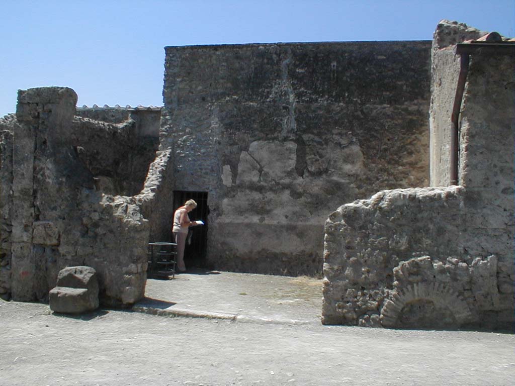 VI.16.6 Pompeii. May 2005. Looking west towards entrance doorway to wide room of fullonica.
According to Sogliano, the entrance doorway threshold was made of lava.
In the left half could be seen a longitudinal track for fixing a board for closure.
In the other half (the right side) the track was missing, and the remains of a hinge proved that there had been a movable shutter of a door there.
In the south-west corner of the west wall is a doorway into what now appears to be a corridor leading to VI.16.7.
According to Sogliano, this actually led into a narrow room which was under the stairs from the peristyle of VI.16.7.
See Notizie degli Scavi di Antichità, 1906, p. 350.