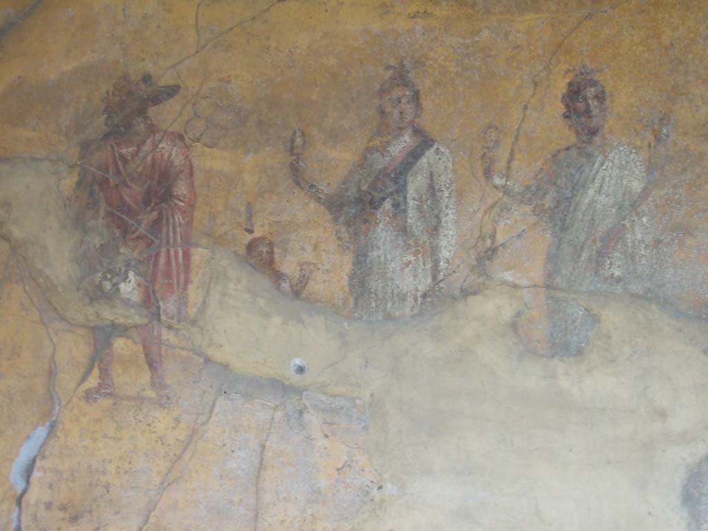 VI.16.7 Pompeii. May 2006. Room F, painting of gods on the south wall of the peristyle.  
Isis is in the centre wearing a red and black sash and holding a sistrum.  
Anubis is dressed in red. A small figure between Isis and Anubis is possibly Harpocrates.  
Serapis or Osiris is dressed in white with the horn of plenty in his left hand and a sistrum in his right.  
See Fröhlich, T., 1991. Lararien und Fassadenbilder in den Vesuvstädten. Mainz: von Zabern. (L74, T. 38,1-2).