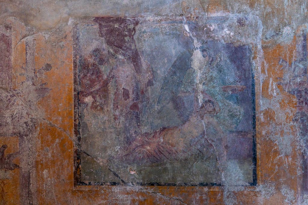 VI.16.15 Pompeii. January 2024. 
Room G, central painting of the arrival of Dionysus on Naxos where Ariadne is sleeping, from west wall. Photo courtesy of Johannes Eber.
Kuivalainen describes –
“A composition of at least six figures; the two on the right are in an arching cave-like space, marked with dark brown. In the foreground, a female reclining to the right, raises her right arm to the top of her head as if awakening; a pink cloak covers her legs. Behind her stands a figure with green wings, dressed in a green robe, holding branches in her right hand and a large patera in her left. On the left side of the picture stands a youth stretching his right arm to the left, with a red cloak covering his left shoulder; in his left hand he holds a thyrsus. Behind are members of the thiasus, perhaps with Silenus on the left.”
Kuivalainen comments –
“Another version of the same theme, but Bacchus now seems to be paying less attention to the awakening Ariadne.”
See Kuivalainen, I., 2021. The Portrayal of Pompeian Bacchus. Commentationes Humanarum Litterarum 140. Helsinki: Finnish Society of Sciences and Letters, (p.148, E10).
