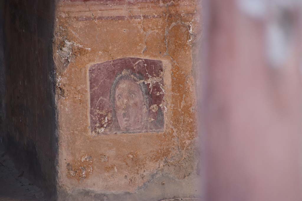 VI.16.15 Pompeii. September 2021. 
Atrium B, wall painting of face or mask between doorway to room E and room D at base of pilaster. Photo courtesy of Klaus Heese.