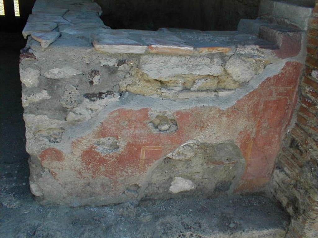 VI.16.33 Pompeii. May 2005. Remaining painted plaster on west-facing exterior side of counter. According to NdS, the outer surface of this counter had a red background. On the surface facing the road, according to Sogliano, obscene paintings were discovered. In the centre, in a yellow frame, was a large erect phallus. On each side, a male figure could be seen facing towards the centre panel and each other. The figure on the right was better preserved, and bald. There were also other painted panels and arabesques.See Notizie degli Scavi di Antichitŕ, 1908, (p.289).