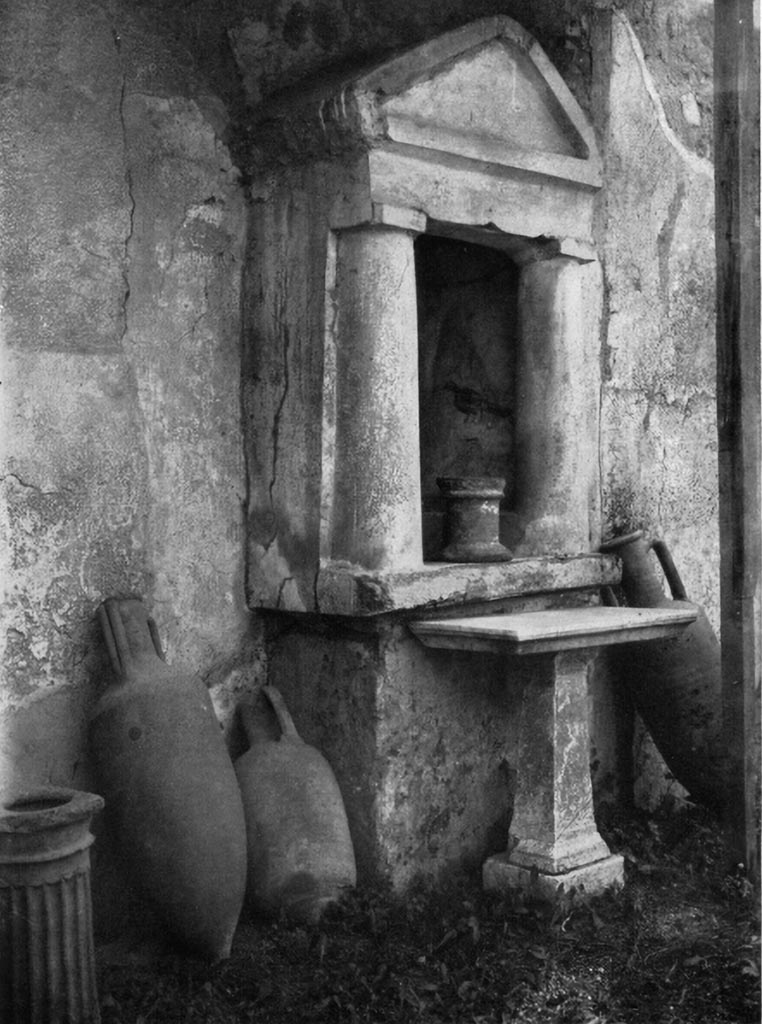 VI.16.36 Pompeii. Photo by Tatiana Warscher (c.1930s). Lararium (b) on south wall of peristyle.
According to Boyce, against the south wall of the peristyle stood an aedicula of unusually heavy proportions.
Above a rectangular podium and before a rectangular niche cut into the walls, stood two thick and heavy columns.
The inside walls of the niche were coated with white stucco and upon each painted a large bird holding something in its beak.
Above them were garlands.
On the ground in front of the aedicula stood a table of white marble with travertine support.
Within the shrine were found two large terracotta lamps.
See Boyce G. K., 1937. Corpus of the Lararia of Pompeii. Rome: MAAR 14. (P.59, no.229, and Pl.33,2). 
See Fröhlich, T., 1991. Lararien und Fassadenbilder in den Vesuvstädten. Mainz: von Zabern. (L76, Picture 39,3, painting in niche very faded).
See Giacobello, F., 2008. Larari Pompeiani: Iconografia e culto dei Lari in ambito domestico. Milano: LED Edizioni. (p.278).
See Notizie degli Scavi di Antichità, 1908, p. 364. (Note that Boyce quotes p.264 in error).