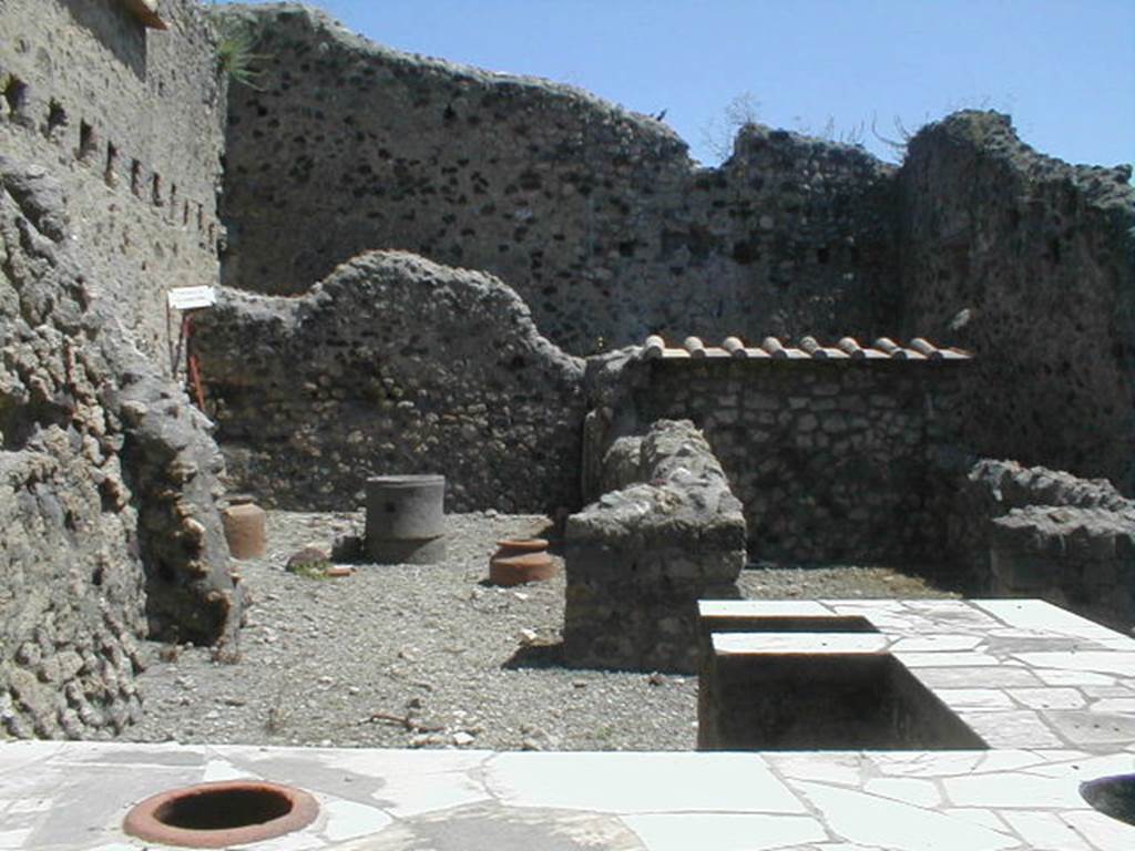VI.16.40 Pompeii. May 2005. Room B, looking east across counter towards two rear rooms C and D and a corridor E to rear, leading to rooms F and G. According to NdS, room B was the bar-room, around which were smaller rooms. Adjacent to the north wall, near the entrance doorway, was the two-sided masonry sales counter or podium. At the other end  in the centre of the bar-room, it ended with a kitchen oven (a), also in masonry. The external vertical surface of the sales counter was painted in red. The horizontal surface was decorated with embedded triangular slabs of marble and other shapes. Leaning against the north wall were the usual three small masonry steps, painted in red, to display the goods and housewares. The room was rather rustic.
At the east end of the north wall of the bar-room, near the doorway to room C, was a doorway to the area below the stairs at VI.16.39. Rooms C and D were rooms for the use of the clients of the bar. When excavated, the entrance doorposts on the left showed the imprint left by the timber. At the north end of room G, behind room C, was the latrine (b).