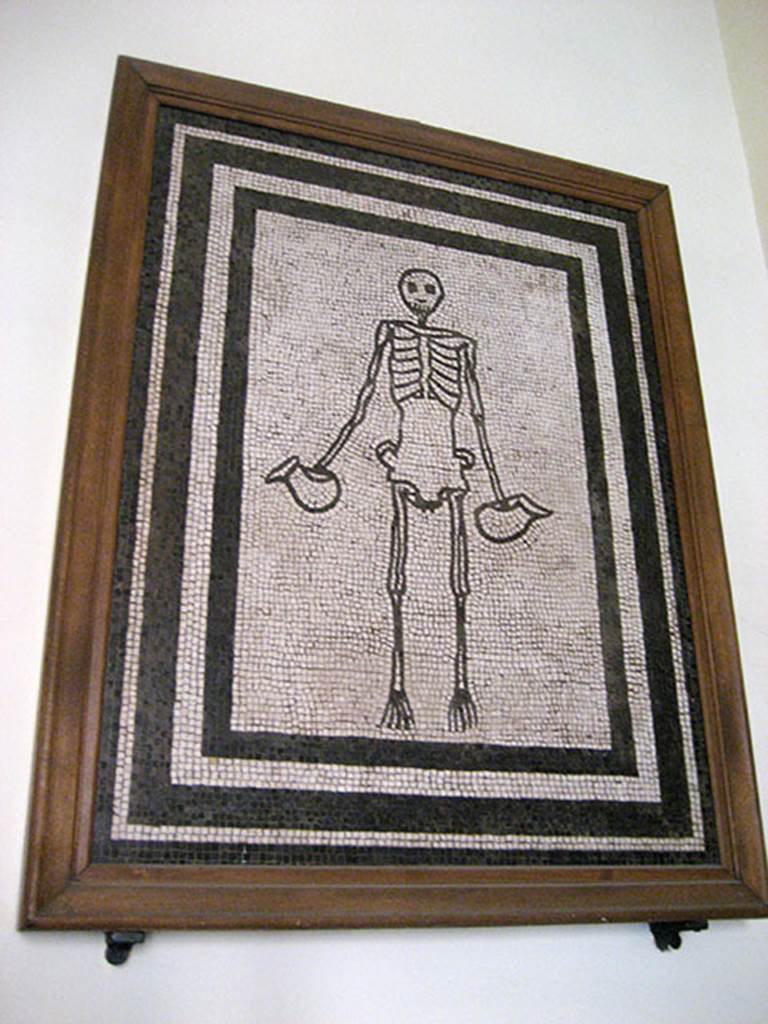 VI.17.19-26 Pompeii. Found in the week to 17th May 1783 in a room of a lower apartment. Mosaic of skeleton holding a jug in each hand.
Now in Naples Archaeological Museum.  Inventory number 9978.
The parts of the walls that remained were painted black. In the middle was a red panel in which were painted some figures. 
The room had a window with a threshold of ordinary white mosaic and here rested clearly a skeleton that held in each hand a jug made with black mosaic. 
The floor of this room was of ordinary white mosaic with some black bands around it and many items of bronze, terracotta, glass, bone were found here.
See Pagano, M. and Prisciandaro, R., 2006. Studio sulle provenienze degli oggetti rinvenuti negli scavi borbonici del regno di Napoli.  Naples: Nicola Longobardi, p. 80.