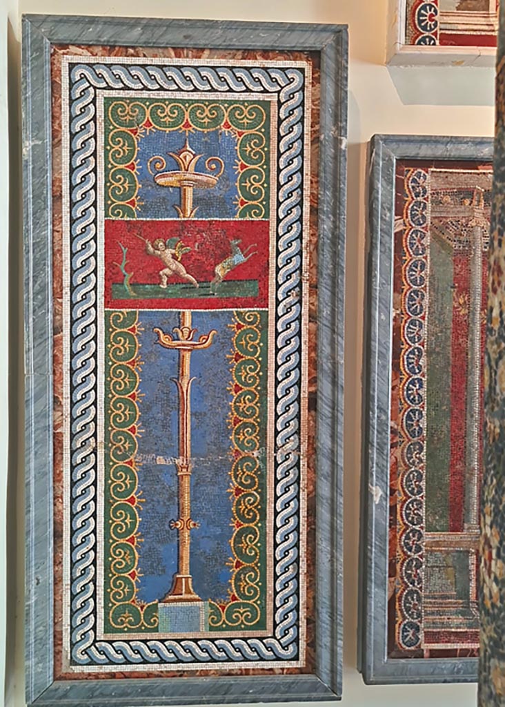 VI.17.36 Pompeii. September 2024. 
One of two mosaic wall panels, now in Naples Archaeological Museum. Inv. no. 10012 and 10013.
Photo courtesy of Giuseppe Ciaramella.
According to the information card –
Mosaic wall panels made from polychrome glass paste tesserae on a light blue background with a gilt candelabrum.
Above, a cupid hunting a deer is depicted within a small panel with a red background, enclosed within a double frame, the outer one with an interlaced pattern and the inner one with plant motifs. (Third quarter of the Ist century AD).
(Pannelli parietali a mosaico di tessere policromo in pasta vitrea su fondo azzurro, con candelabro dorato. In alto, all’interno di un quadretto a fondo rosso, delimitato da una doppia cornice, esterna a treccia, interna a motivi vegetale, e raffigurato un erote che caccia un cervo. 
Terzo quarto del I secolo d.C.)