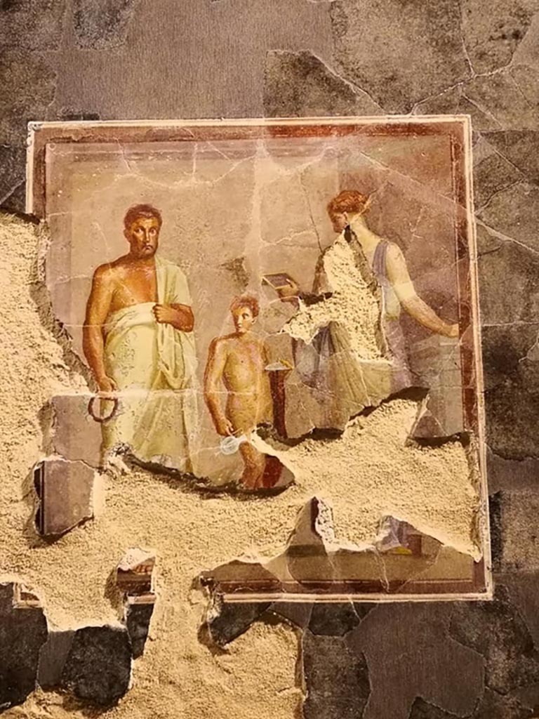 VI.17.42 Pompeii. December 2019. 
Fragments of a dining room fresco from the centre of a wall, thought to be the poet Euphorion.
On display in exhibition “Pompei e Santorini” in Rome, 2019. Photo courtesy of Giuseppe Ciaramella.
A female (poetess?) is reading a diptych, and a boy with a red cloak has a plate for offerings.
Parco Archeologico di Pompei, inventory number 86075. 
This is part of a larger panel, one of several items recomposed from a large number of fragments found in a channel in the garden. 
It is thought to be from the reconstruction work following the damage after the earthquake of AD62. 
Its original room location is unknown.
See Aoyagi M. and Pappalardo U., 2006. Pompei (Regiones VI-VII) Insula Occidentalis. Napoli: Valtrend. (p. 222-7).