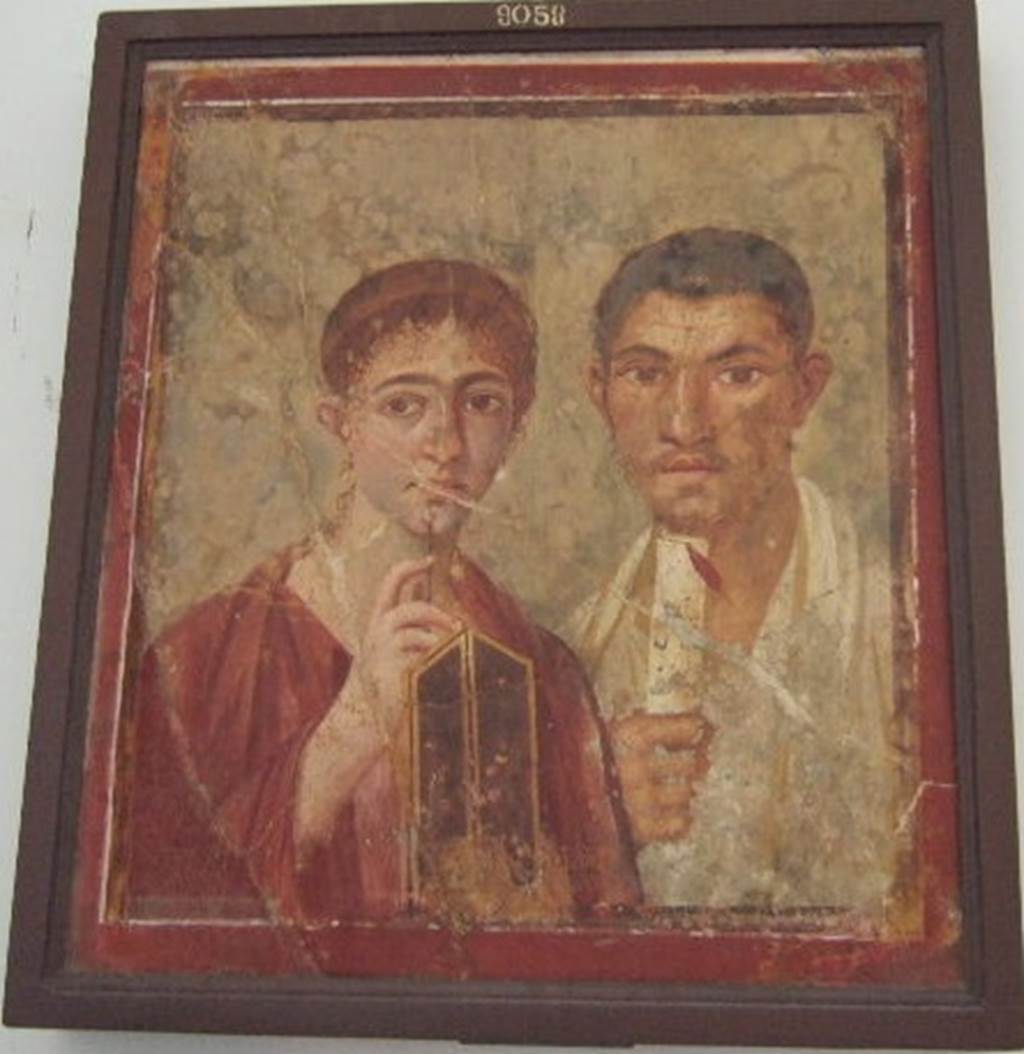VII.2.6 Pompeii. Portrait of Terentius Neo and his wife. Found on north wall of exedra/tablinum in centre of north side of atrium.  Now in Naples Archaeological Museum.  Inventory number: 9058.
In the upper zone of the painted architecture was a fresco of Cupid and Psyche. The red zoccolo showed a painted plant in the centre panel, and painted garlands with peacocks on them in the side panels. In the middle zone of the wall, the central panel was painted white, which separated the two yellow side panels.
In one of these side panels, “but already very faded and nearly vanished” was the painting of “Nike standing on a shelf, and carrying a trophy on his left shoulder”.