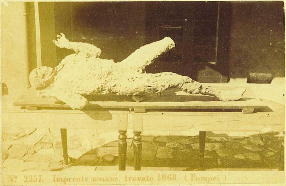 VII.2.16 Pompeii. One of the seven skeletons found in the house on 12th March 1868. Photo courtesy of Rick Bauer. Seven skeletons were found, but six of them had not left enough imprint in the cinders to make a good plaster cast. The above was the only successful one, although his left leg was not cast, on his face was a look of horror.
See Garcia y Garcia, L., 2006. Danni di guerra a Pompei. Rome: L’Erma di Bretschneider. (p.190)
According to Dwyer, the cast was only partially successful as the cavity had been infiltrated by lapilli and this left the skull and left leg exposed.
This cast, known as the Fifth Victim, was placed in the Archaeological School, and it was here that Ernest Breton saw it, and described
“This unfortunate was discovered lying on his stomach in a room to the left of the atrium of the House of Gavius Rufus.  Six other skeletons were near him”  from Breton, 1869.
See Dwyer, E., 2010. Pompeii’s Living Statues. Ann Arbor: Univ of Michigan Press. (p. 80)