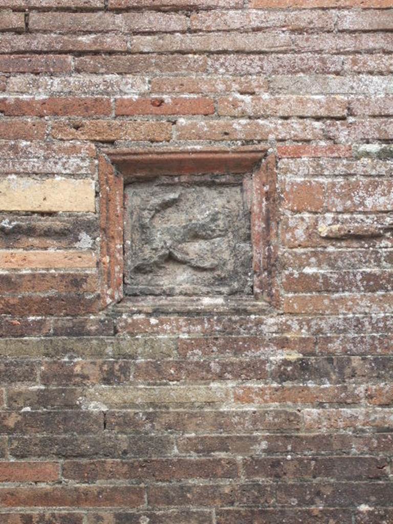 VII.2.32 Pompeii. May 2006. Plaque showing a flying phallus, on wall between VII.2.31 and VII.2.32. According to Della Corte, “a characteristic, complex relief (embedded in the wall to the left of the first entrance) destined to protect the hostelry”.