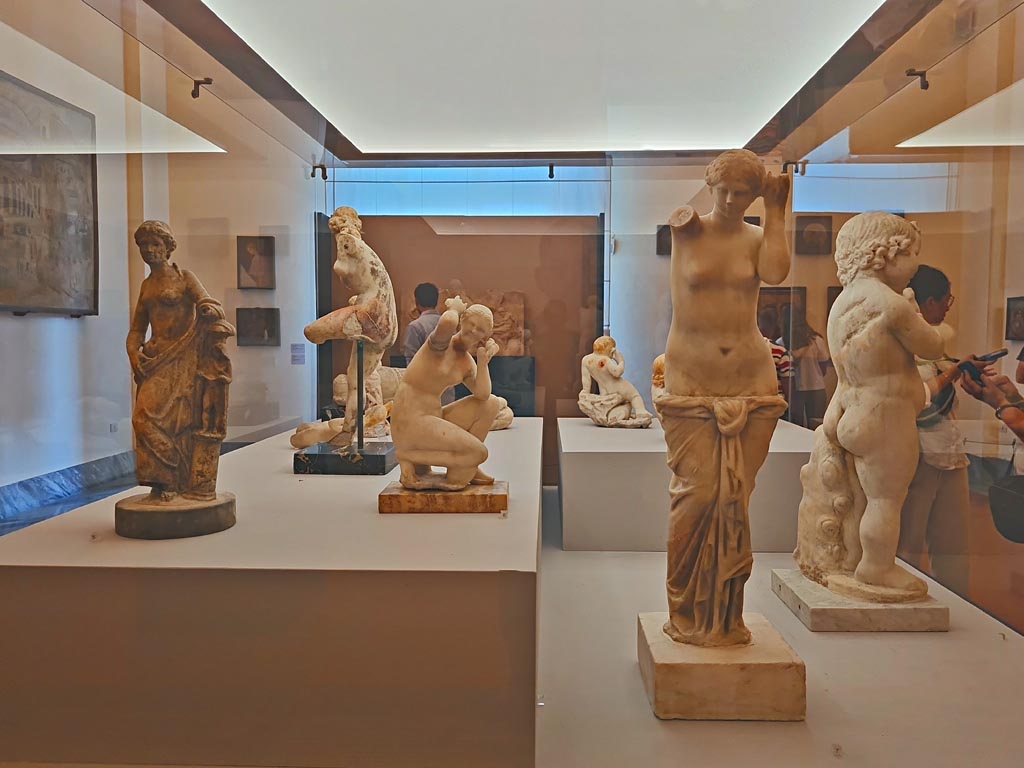 Display in “L’altra MANN” exhibition, October 2023, at Naples Archaeological Museum of Venuses and other garden statuettes.
Centre right is the large Venus found in the aedicula lararium on south wall of garden in VII.3.6, Pompeii. 
Photo courtesy of Giuseppe Ciaramella.