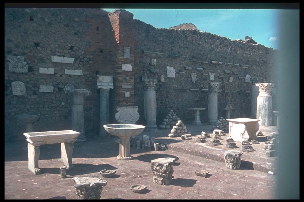 VII.7.29 Pompeii. Items on display and in storage.
Photographed 1970-79 by Günther Einhorn, picture courtesy of his son Ralf Einhorn.
According to Garcia y Garcia, it was Maiuri that restored the pilasters of this building and formed it into a display area.
Mostly these items on display are clay amphorae and domestic items from the houses, shops and workshops.
For the most part without provenance and classified only by type and form.
The bombing of 13th September 1943 caused the demolition of the south perimeter and part of the west wall
At least two of the seven pilasters of the entrance doorways were also demolished.
In 1946 Maiuri again restored the pilasters and roof.
See Garcia y Garcia, L., 2006. Danni di guerra a Pompei. Rome: L’Erma di Bretschneider. (p.116-7)